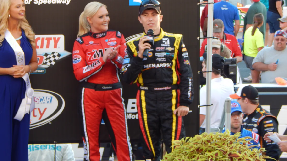 Stock Car Racing Driver Suit Accessories Modern stock car racing driver in full sponsor uniform standing next to his race car